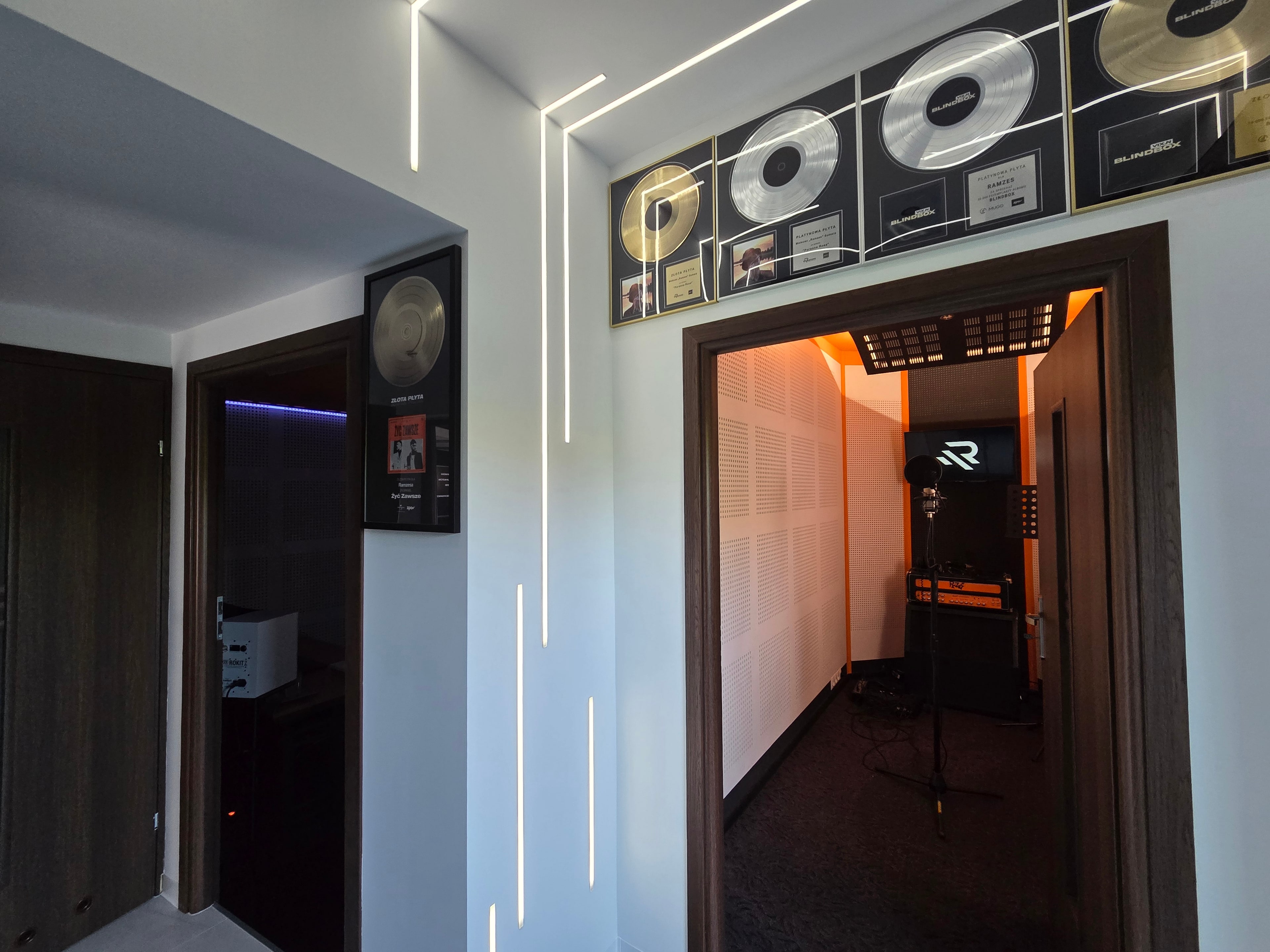 Korytarz Ramzes Studio, ściana z płytami i wejście do oświetlonej kabiny nagraniowej